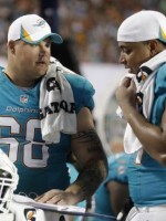 Two linemen in Dolphin turquoise jersies w/o helmets talk to one another off field
