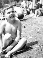 Very young boy in suit sitting on beach frowing