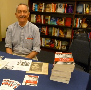 Karl Schonborn sitting at bookstore table w stack of books.
