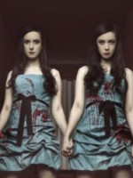 The SOSKAS twin sisters hold hands in a hallway with a bloody axe imbedded in a wall.