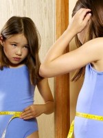 Lookism? Little girl with tape measure around her waist looks into mirror.