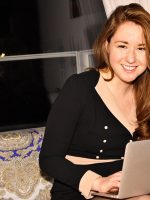 Woman with bronze laptop computer on lap.
