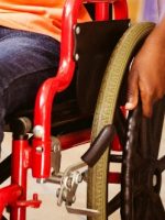 Closeup photo of wheelchair with red frame and black hand on large wheel.