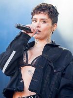 Dark-haired, black-clothed bust shot of cyberbullying victim Kehlani singing into mic.